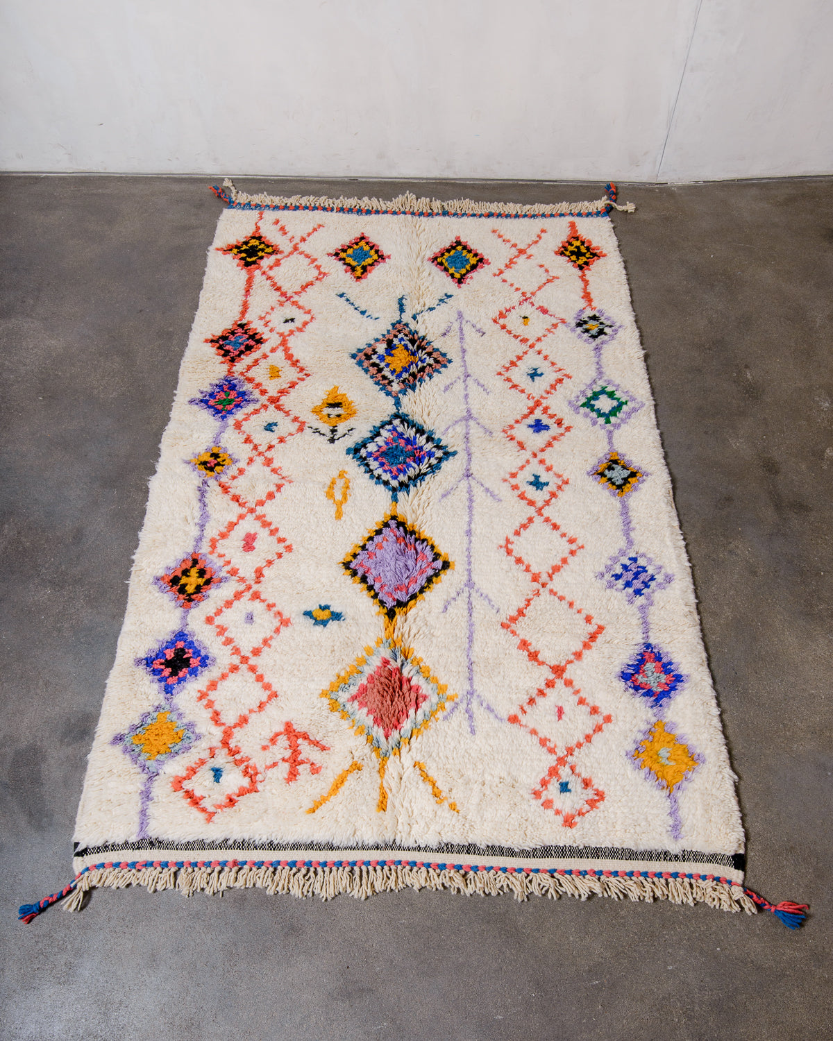 Berberlin Beniourain rug in colourful wool and cream, laying flat on concrete studio floor.